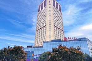 A tall, modern building with a glass facade and a prominent red sign on the top. - Huatian Hotel (Xiangtan)