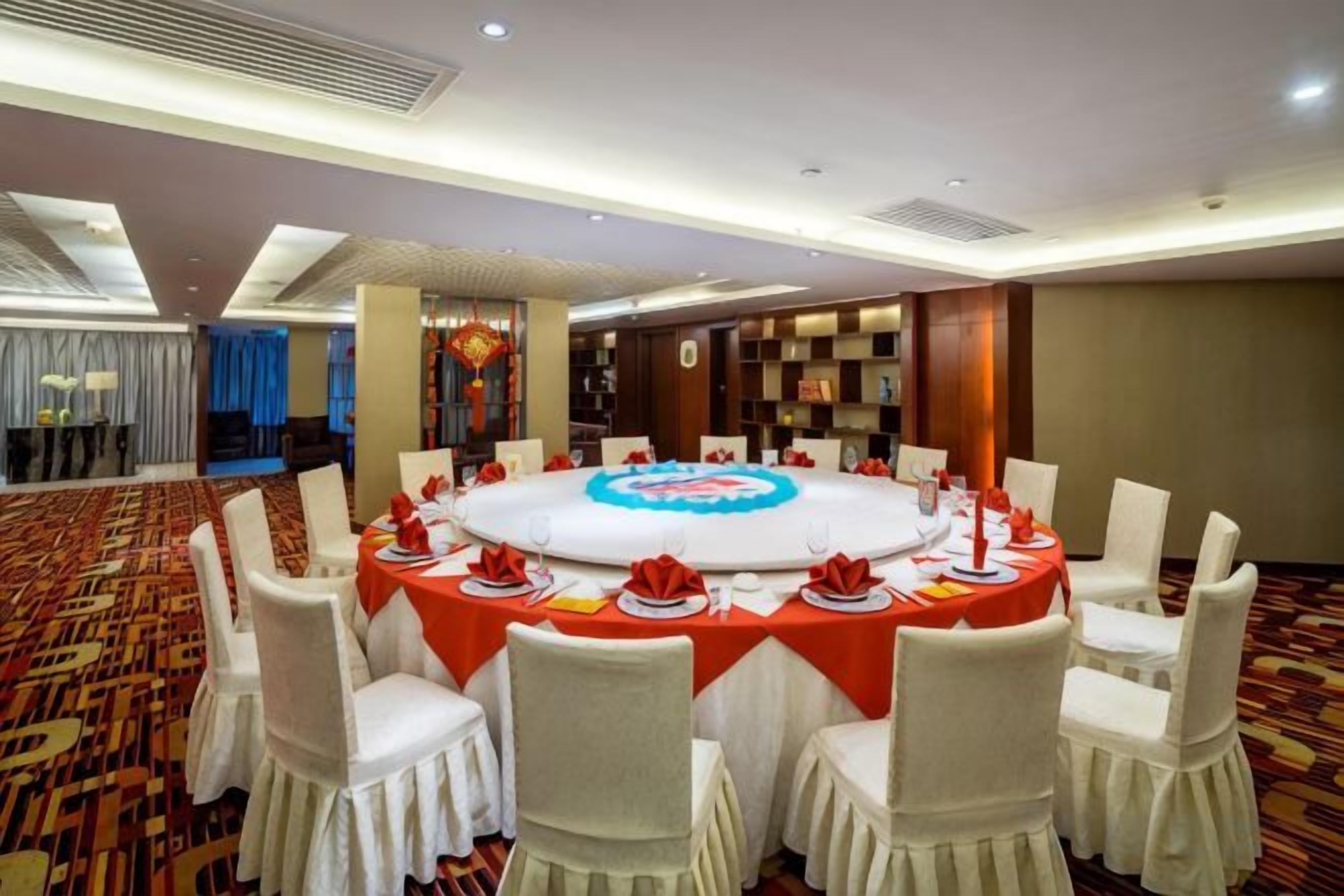 A conference room with a round table, white chairs, and a red tablecloth.