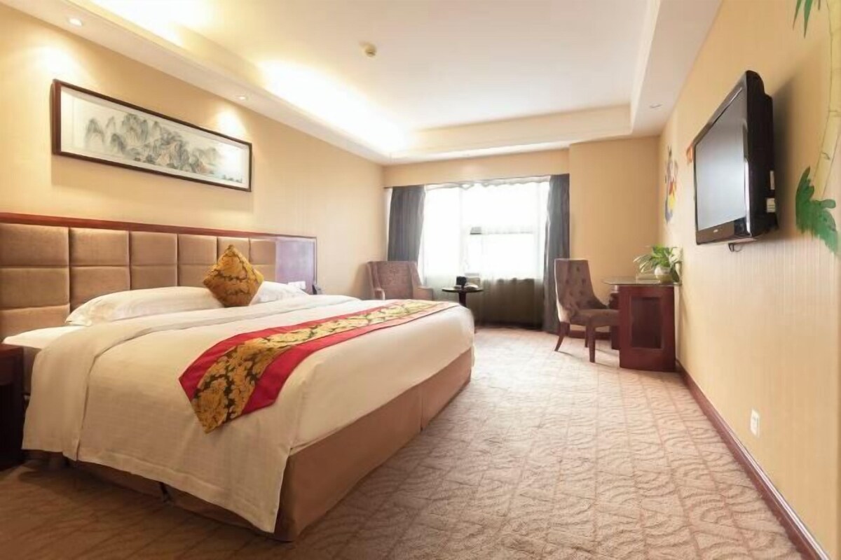 A hotel room with a large bed, a television, a desk, and a chair.