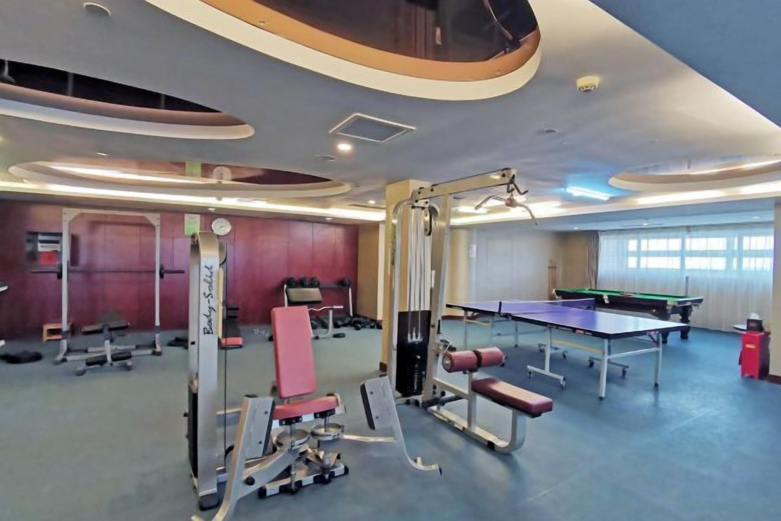 Uma academia com equipamentos de exercícios, uma mesa de pingue-pongue e uma mesa de bilhar.
