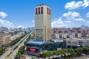 Un edificio de gran altura con diseño moderno, rodeado por un paisaje urbano con otros edificios y un cielo despejado.
