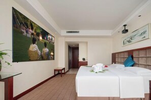A hotel room with a large bed, a small table, a chair, a painting on the wall, and a door leading to another room. - Huatian Hotel (Xiangtan)