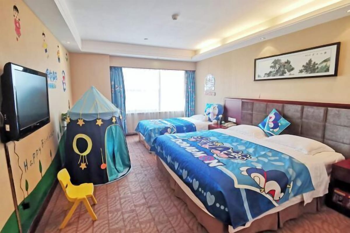 A hotel room with two beds, a TV, a small play tent, and a framed picture on the wall.
