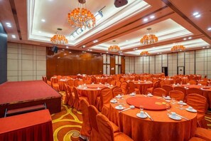 A banquet hall with round tables, orange tablecloths, and a stage area. - Huatian Hotel (Xiangtan)