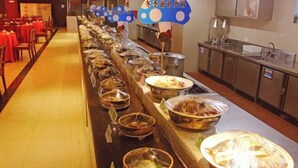 En buffet med forskellige retter i skåle og under overdækkede beholdere, en vask samt en bordplade med bestik.