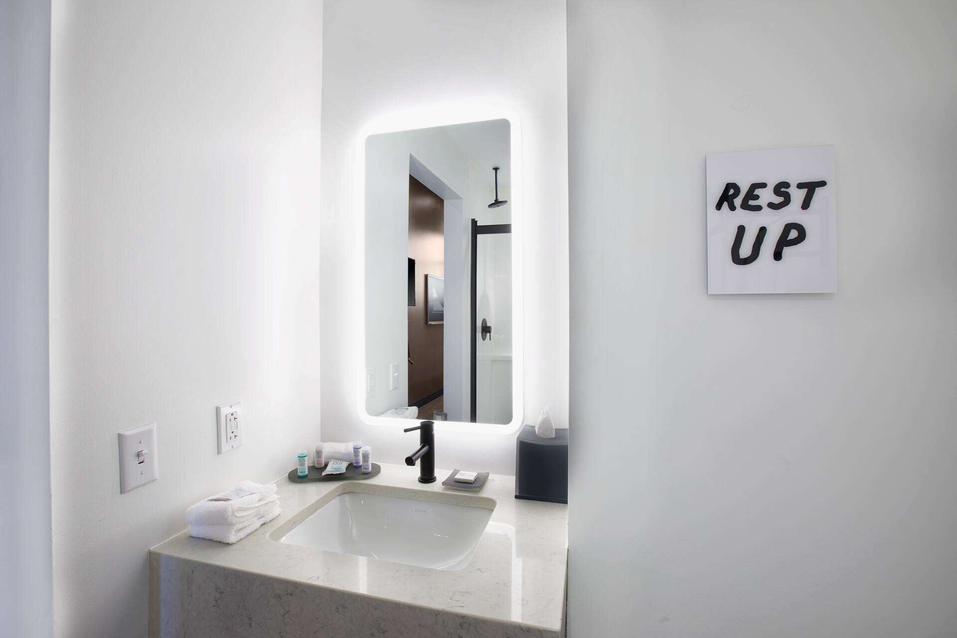 Een badkamer met een wastafel, spiegel en een bordje met de tekst 'REST UP'.