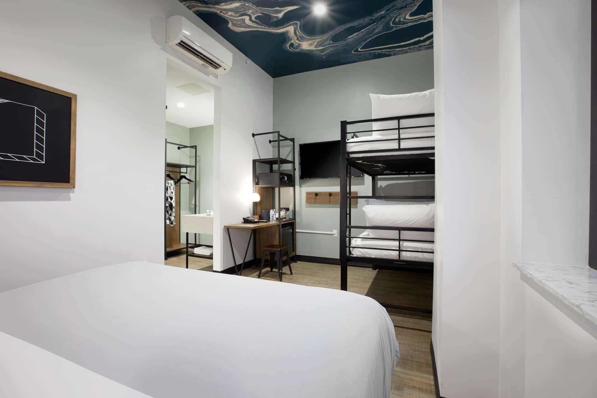 Una habitación de hotel moderna con literas, un escritorio con silla, un espejo y un cuadro en la pared.