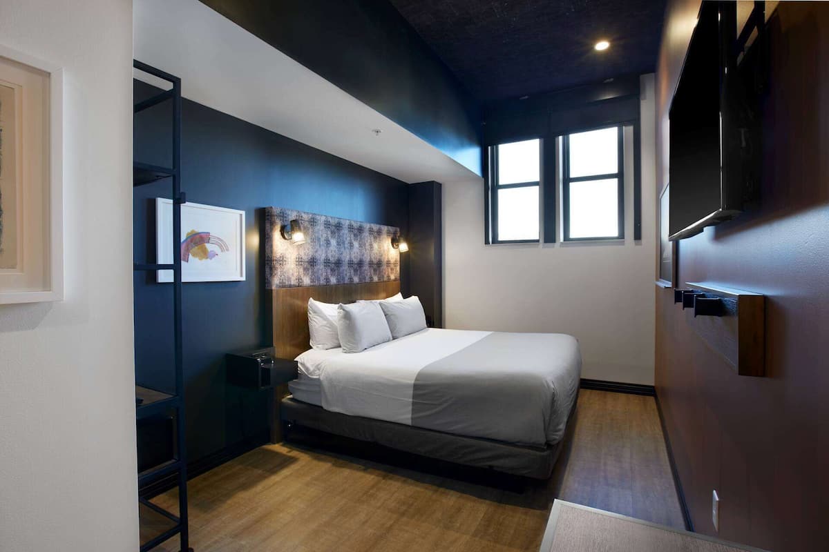 Ein modernes Hotelzimmer mit einem großen Bett, Holzboden, einer dunkel gestalteten Wand und einem Fenster, das für natürliches Licht sorgt.