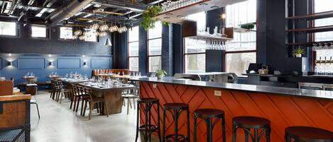 Un restaurante con zona de bar, techos altos y decoración de estilo industrial.