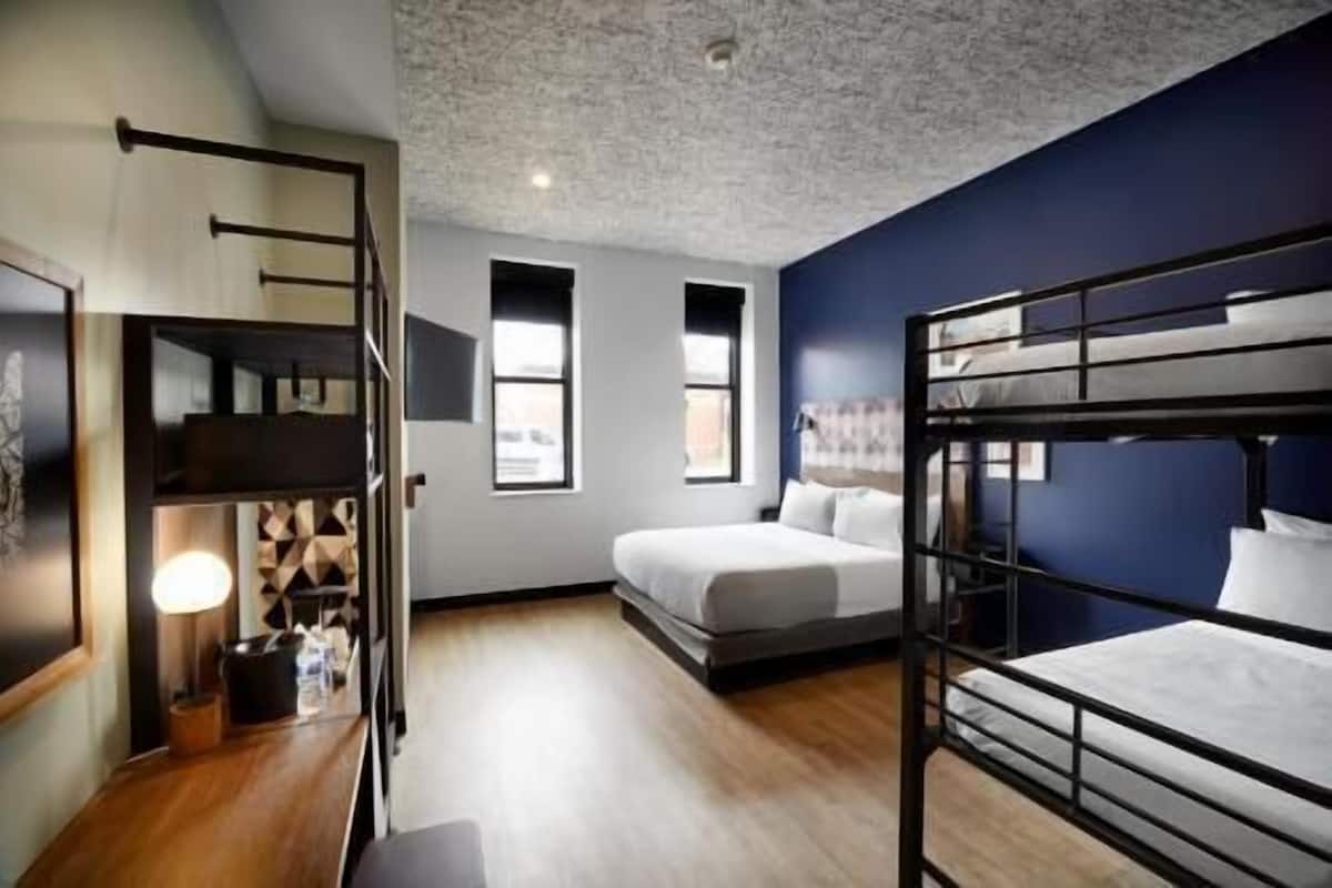 Ein Zimmer mit Etagenbetten, einem Schreibtisch, einem Stuhl, einer Lampe und einem Fenster.