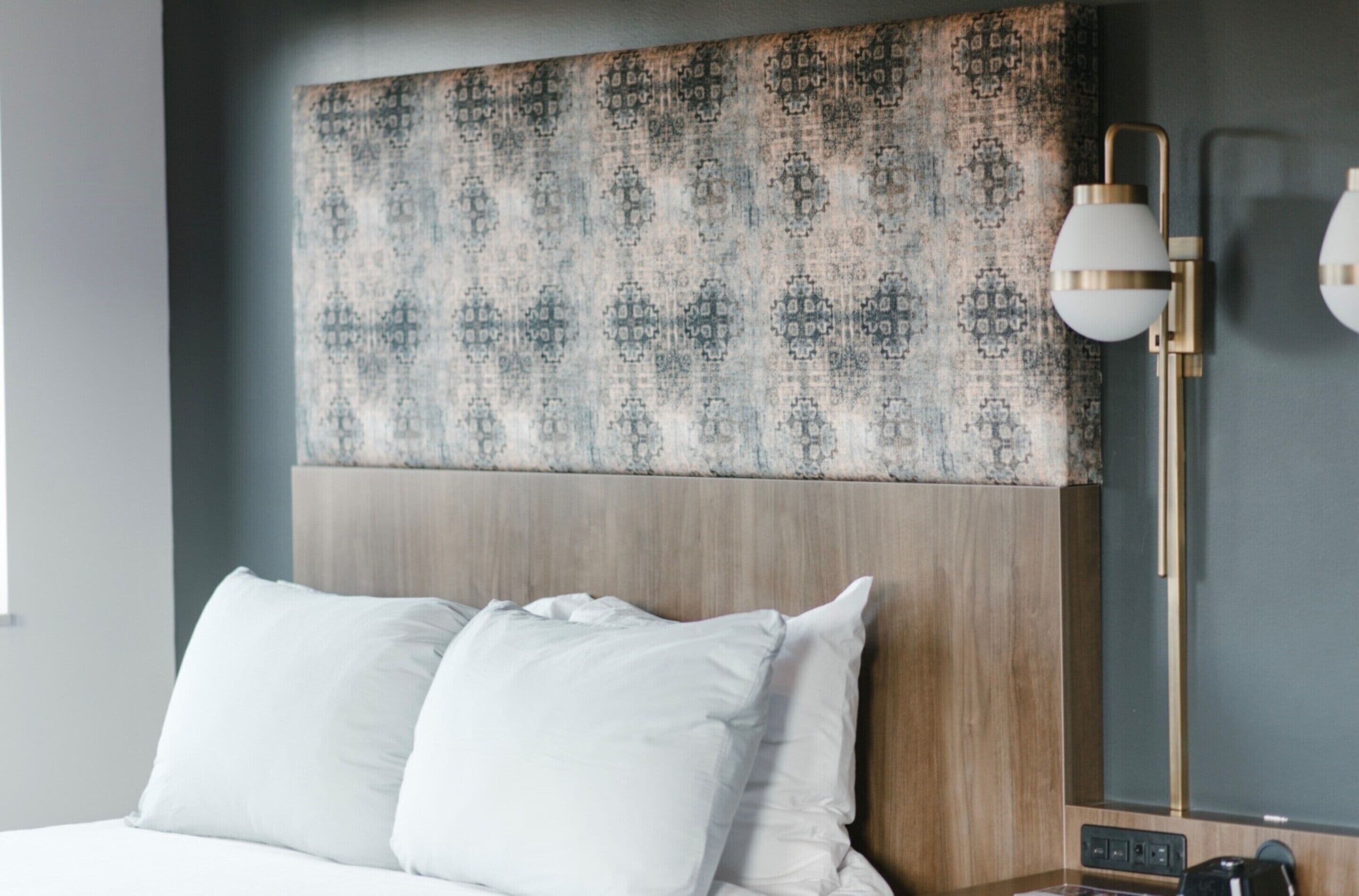 Una habitación de hotel con un cabecero estampado, una lámpara de noche y una cama con almohadas blancas.