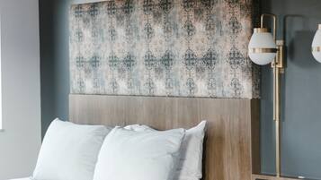 Una habitación de hotel con un cabecero estampado, una lámpara de noche y una cama con almohadas blancas.