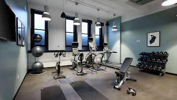 Un gimnasio con equipo de ejercicio, mancuernas y ventanas amplias.