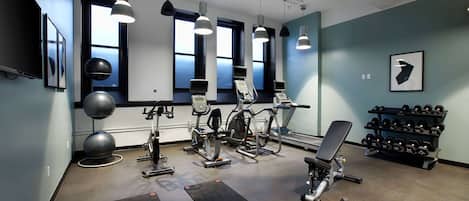A gym with exercise equipment, dumbbells, and large windows.