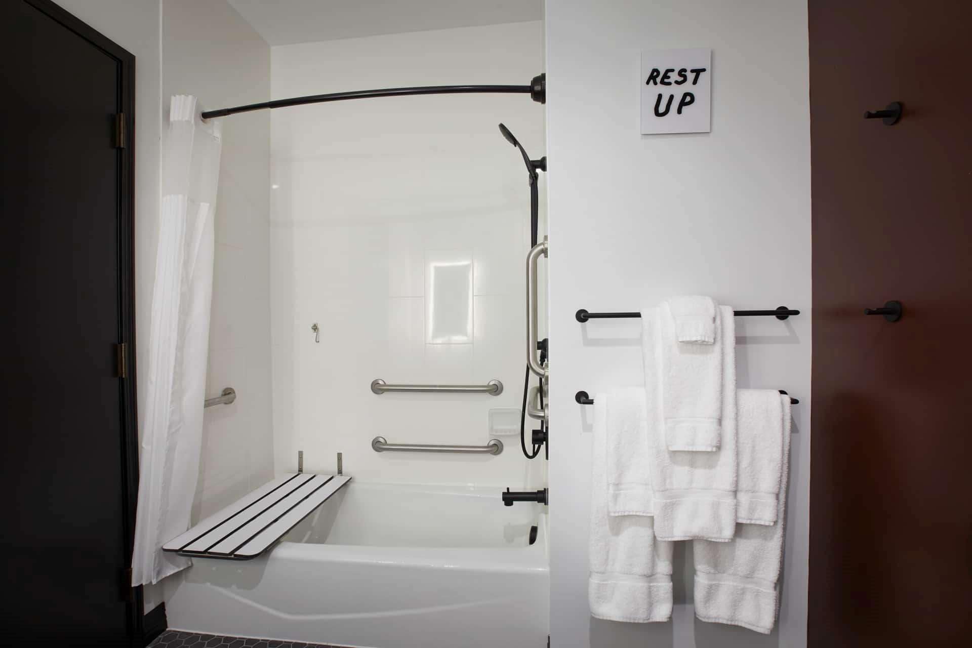Un baño moderno con ducha envuelta en cristal, una bañera y un perchero con varias toallas.