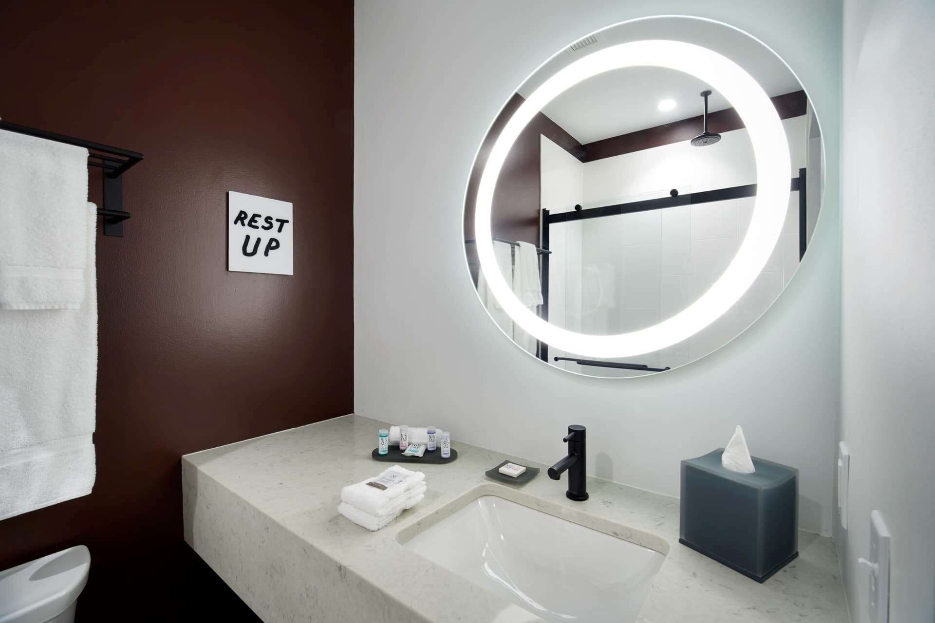A bathroom with a round mirror, a sink, a toilet, and a 'REST UP' sign.