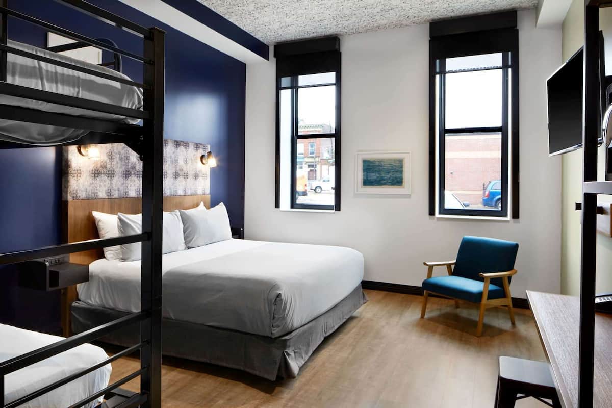 Ein modernes Hotelzimmer mit einem Etagenbett, einem Einzelbett, einem Schreibtisch und einem Stuhl.