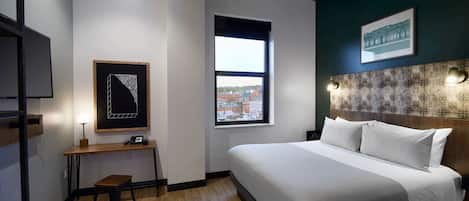 Habitación de hotel con una cama grande, un escritorio con una silla, un ventanal con vista a la ciudad y un techo con diseño que imita el mármol.