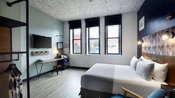 A modern hotel room with a large bed, a desk, and a TV.