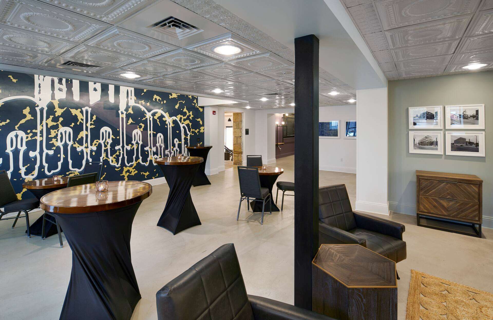 A modern lounge area with round tables, black leather chairs, and a large abstract mural on the wall.