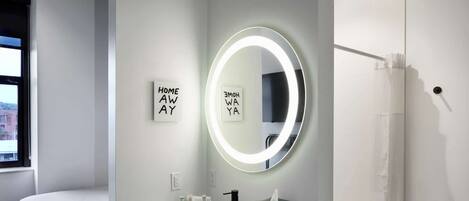 Un baño moderno con un espejo redondo, un lavabo y un perchero para toallas. Hay dos carteles enmarcados en la pared que dicen “HOME AWAY” y “HOME WAY”.