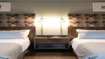 A hotel room with two beds, a nightstand with a lamp, and artwork on the walls.