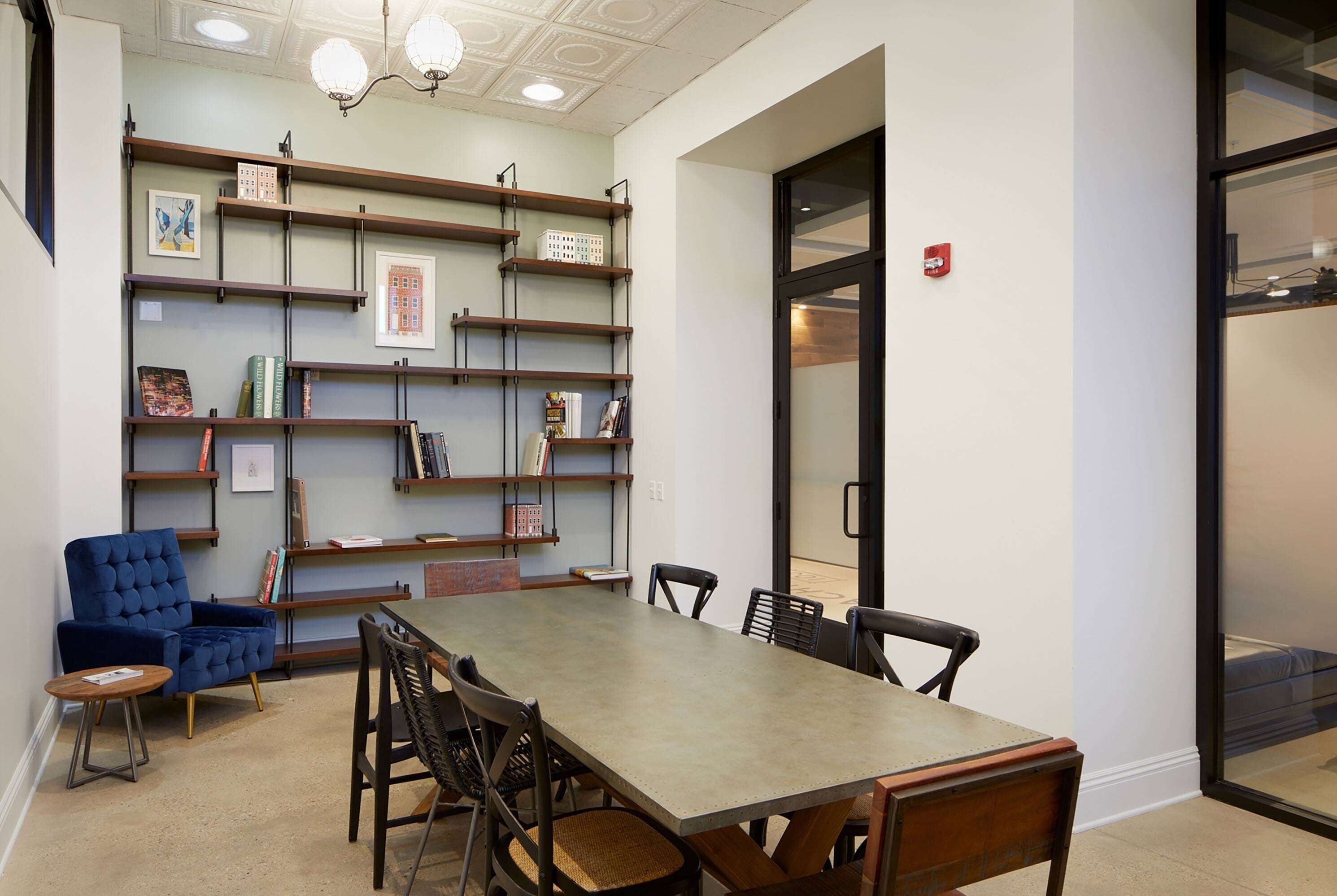 A conference room with a long table, chairs, a blue armchair, and a bookshelf with framed pictures and books.