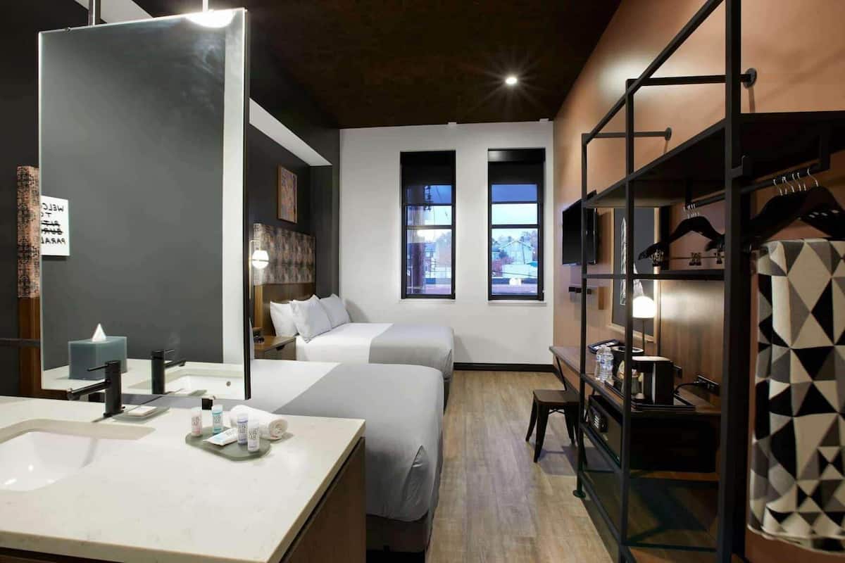 Ein Hotelzimmer mit einem großen Spiegel, zwei Betten, einem Schreibtisch, einem Kleiderschrank und Blick nach draußen.