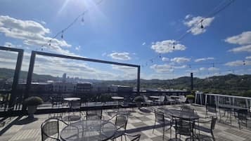 An outdoor patio with tables and chairs, string lights, and a view of a cityscape and hills in the background.