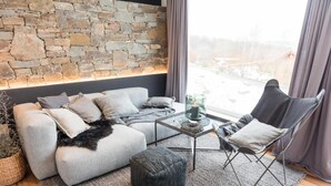 Ein modernes Wohnzimmer mit Steinwand, grauem Sofa, schwarzem Hocker und einem Glastisch.
