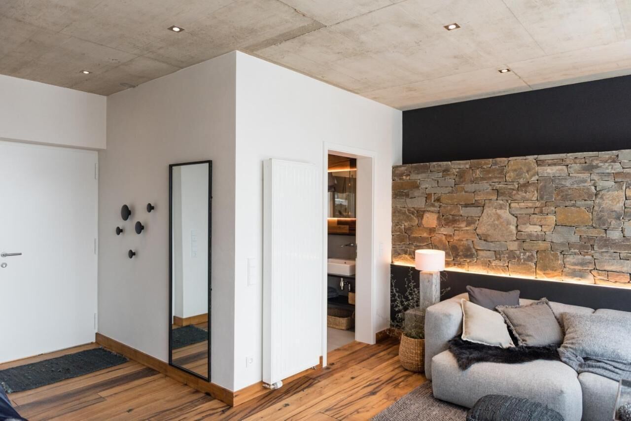 Uma sala de estar moderna com parede de pedra, um sofá cinza e piso de madeira.
