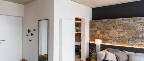 Uma sala de estar moderna com parede de pedra, um sofá cinza e piso de madeira.
