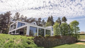 Ein modernes Haus mit großen Glasfenstern, einer Steinwand und einem Rasen.