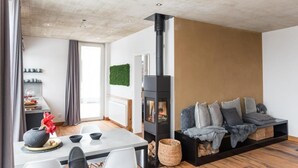 Ein modernes Wohnzimmer mit Kamin, Essbereich mit Tisch und Stühlen sowie eine gemütliche Sitzecke mit Kissen.