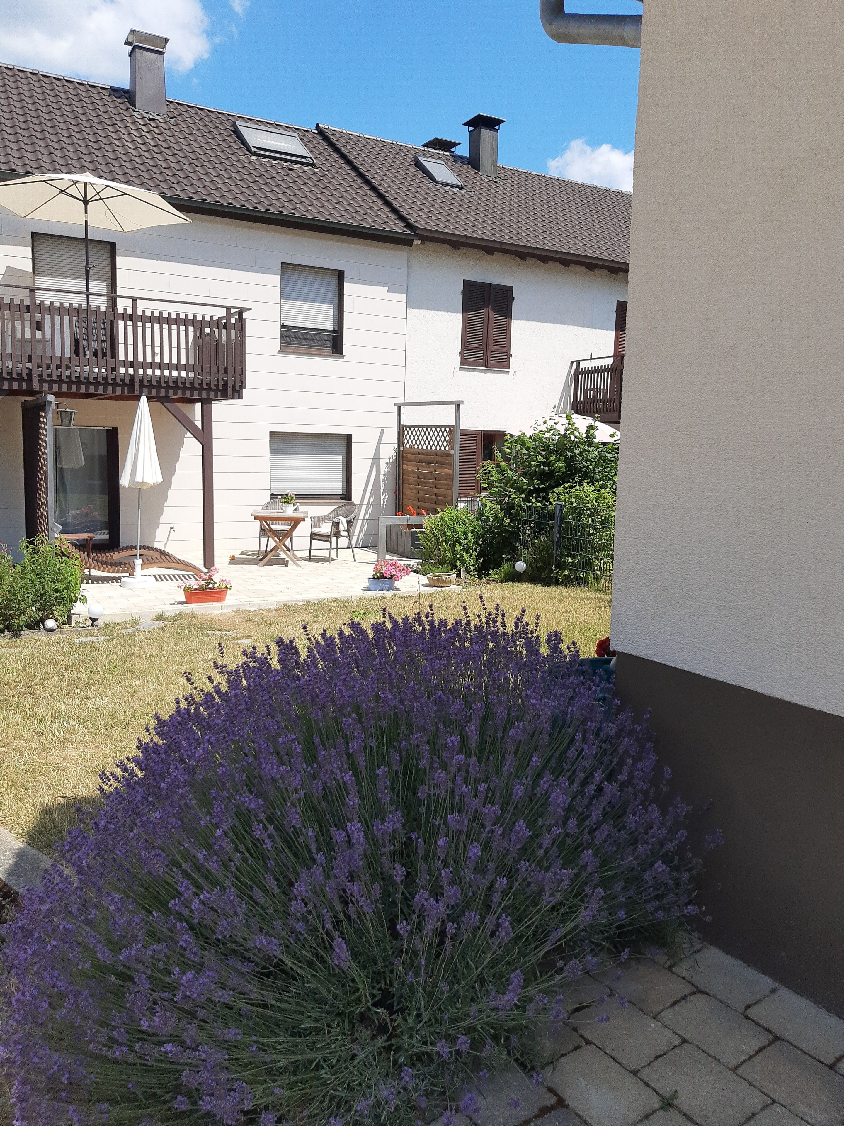 A residential building with a balcony, a patio area with outdoor furniture, and a garden with lavender plants.