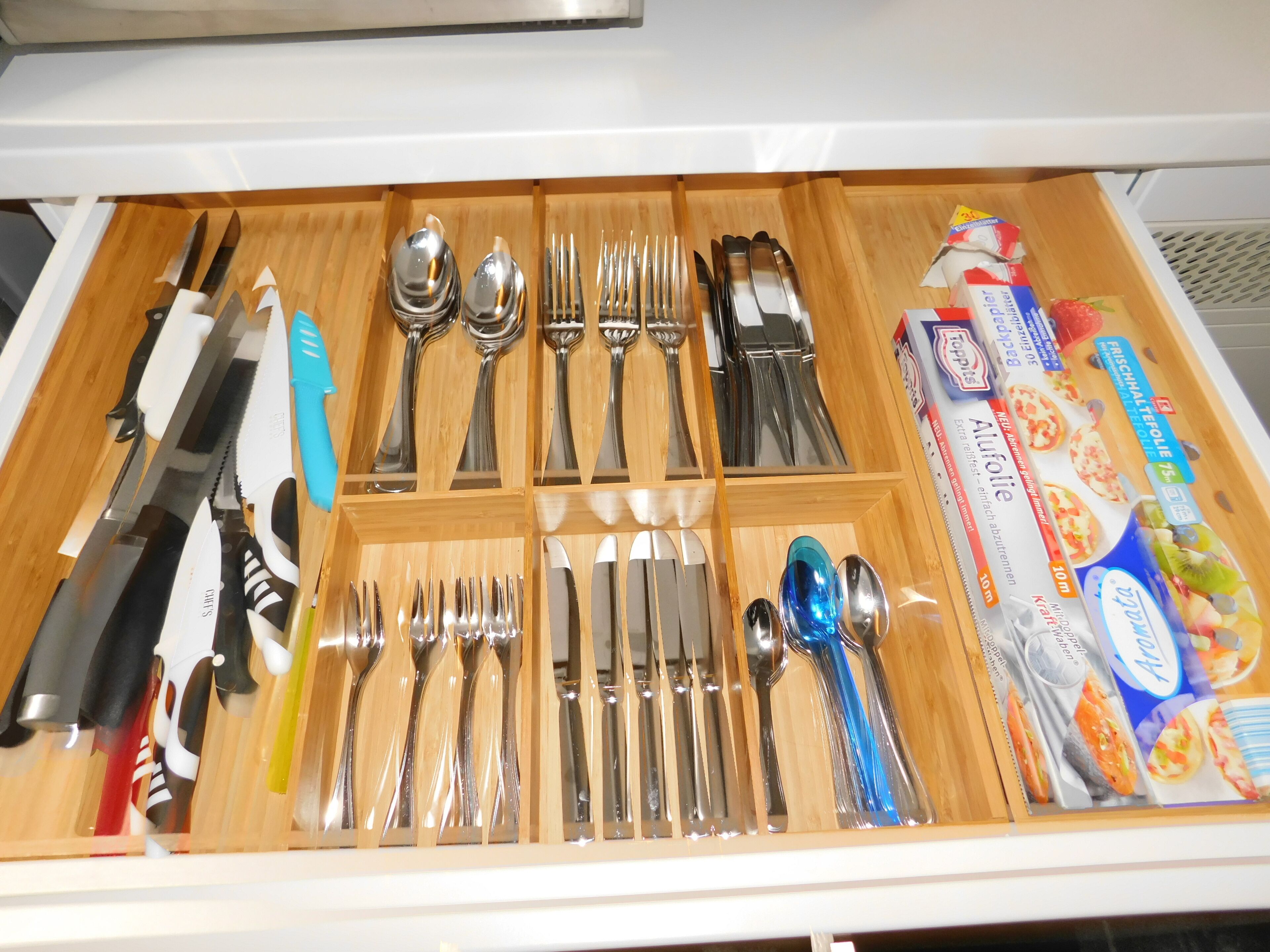 A drawer with neatly organized cutlery including knives, forks, spoons, and a set of chopsticks.