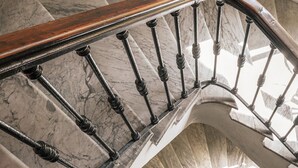 Una escalera de mármol con barandilla de madera y balaustres de metal.
