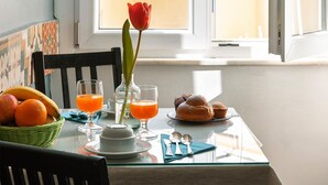 Una mesa de comedor con alimentos para el desayuno, una rosa roja y vistas a un balcón con edificios.