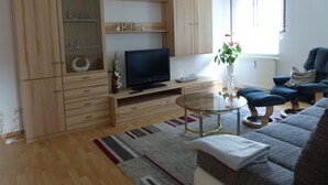 Un saló amb televisió de pantalla plana, armaris de fusta, una taula de cafè de vidre, un sofà i una planta en test.