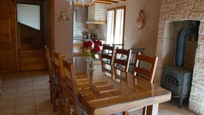 A dining area with a wooden table and chairs, a vase with flowers, and a stone wall stove. - house sleeps 10 4 * (Villard-De-Lans)