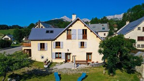 A two-story house with a sloped roof, multiple windows with shutters, and a front porch with a bench. - house sleeps 10 4 * (Villard-De-Lans)