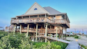 A multi-story wooden house with a balcony, elevated on stilts, surrounded by greenery. - My ReWard Sunset House has a 450’ pier with boat slips, crabbing, fishing, swim (Grand Isle)