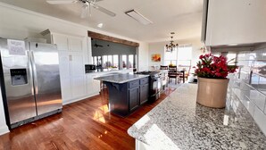 A modern kitchen with stainless steel appliances, a granite countertop, and a wooden floor. - My ReWard Sunset House has a 450’ pier with boat slips, crabbing, fishing, swim (Grand Isle)