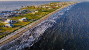 An aerial view of a coastal town with houses along the beachfront, a clear sky, and calm sea. - My ReWard Sunset House has a 450’ pier with boat slips, crabbing, fishing, swim (Grand Isle)