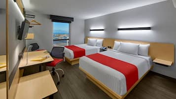 Habitación de hotel con dos camas, un escritorio, una silla, un televisor y una ventana con vistas.