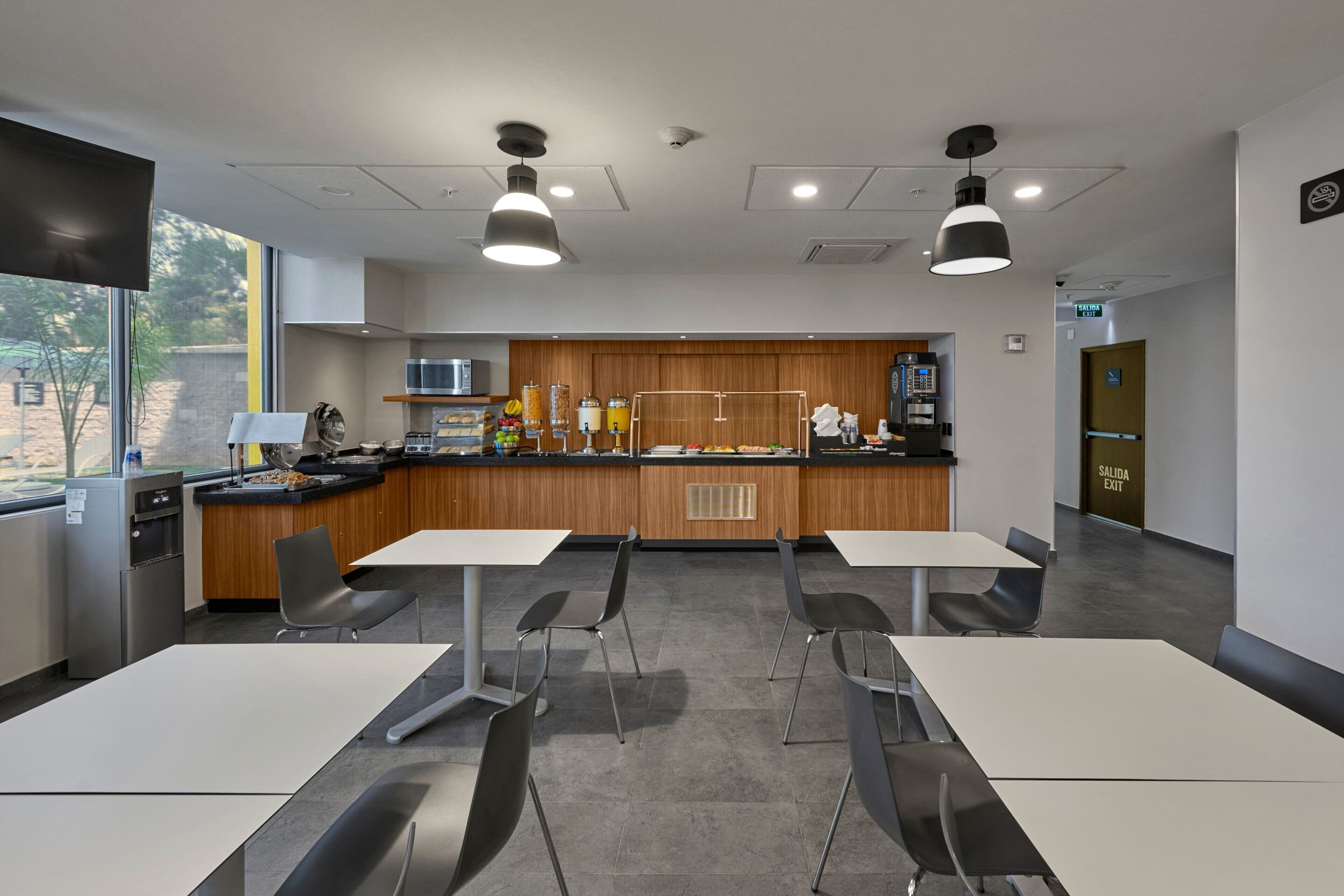 A modern kitchen with a wooden counter, stainless steel appliances, and a large window. There are two tables with chairs in the foreground.
