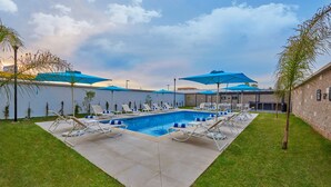 Piscina com espreguiçadeiras e guarda-sóis, cercada por um muro de tijolos e vegetação.