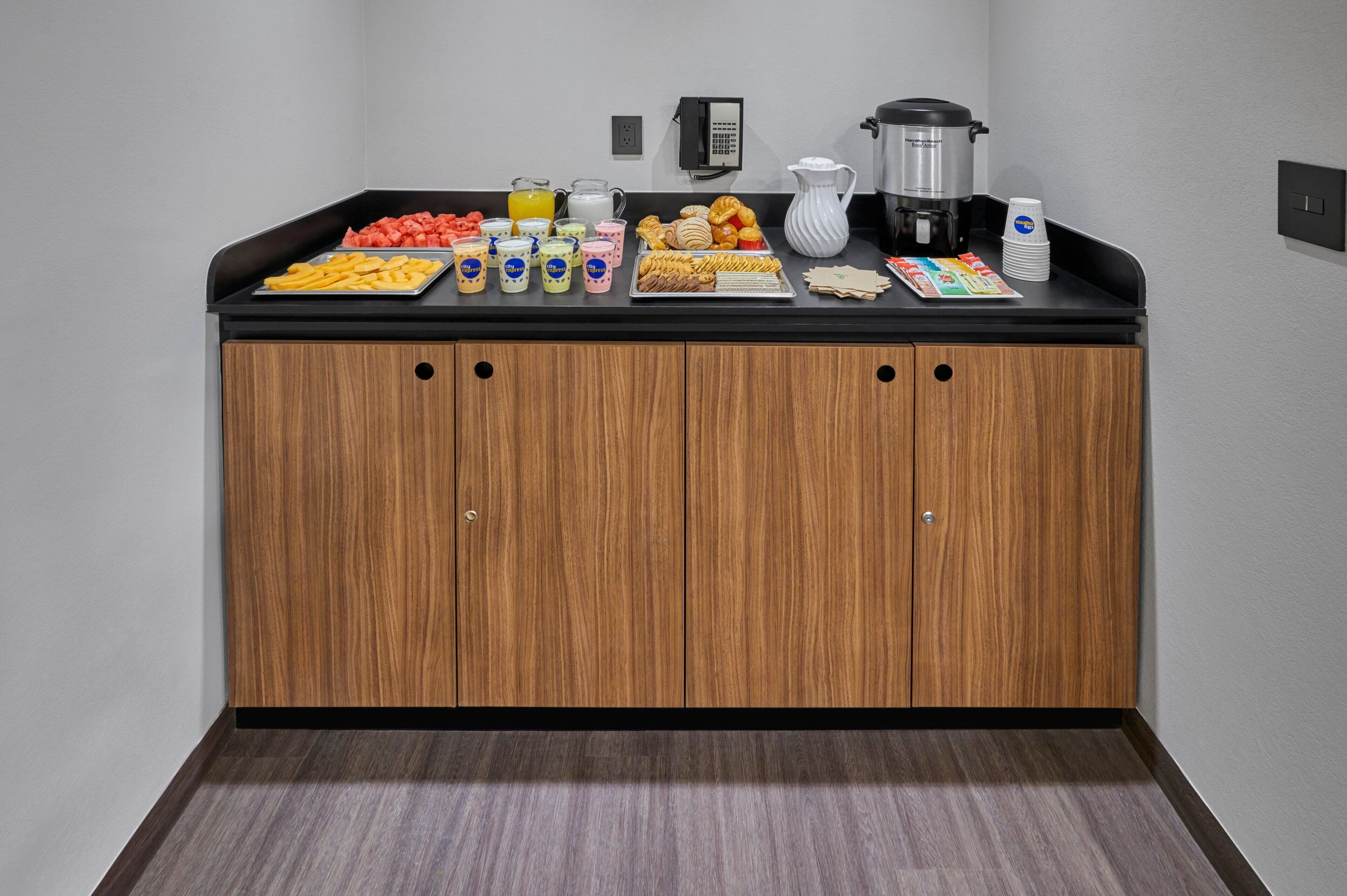 Una kitchenette con encimera negra, armarios de madera y diferentes alimentos y bebidas.