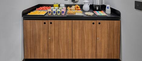 Una kitchenette con encimera negra, armarios de madera y diferentes alimentos y bebidas.
