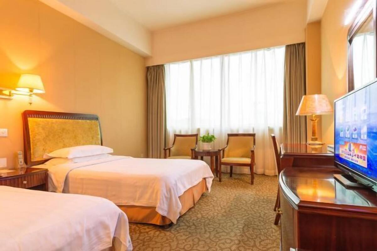 Une chambre d’hôtel avec deux lits, une télévision, un bureau et une fenêtre avec des rideaux.